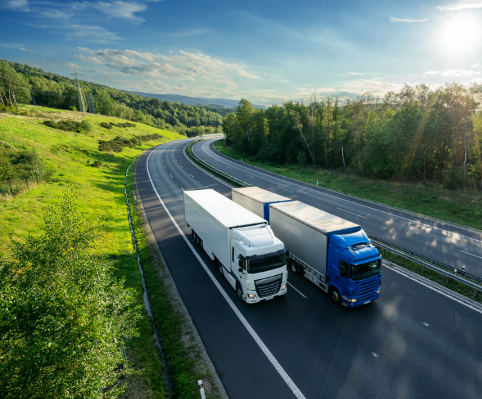 Two trucks on road surrounded by greenery. The image is pleasant and peaceful with the sun shining, all meant to show the significance of sustainable supply chains.