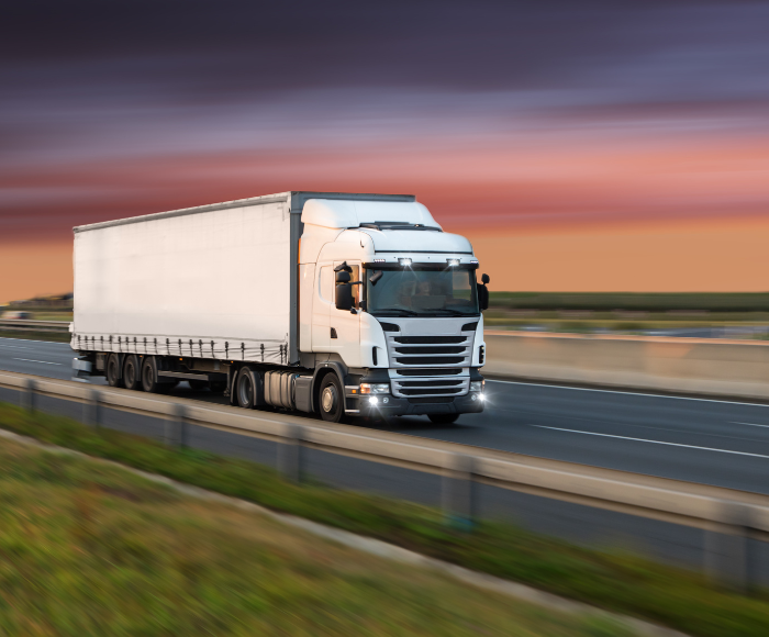 Cargo truck on highway zooms past with purple sky in distance.